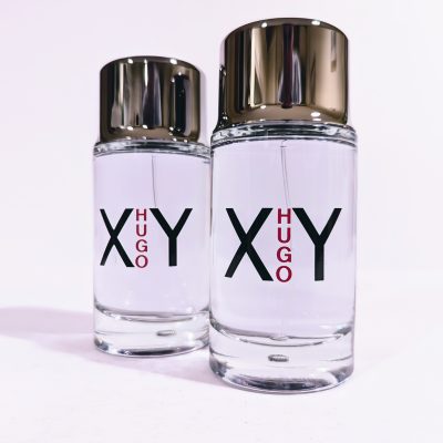 Two clear glass bottles of Hugo XY fragrance, each with silver caps and labels displaying “XY HUGO” in black and red text.