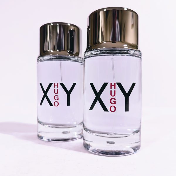 Two clear glass bottles of Hugo XY fragrance, each with silver caps and labels displaying "XY HUGO" in black and red text.