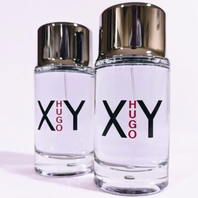 Two clear glass bottles of Hugo XY fragrance, each with silver caps and labels displaying "XY HUGO" in black and red text.