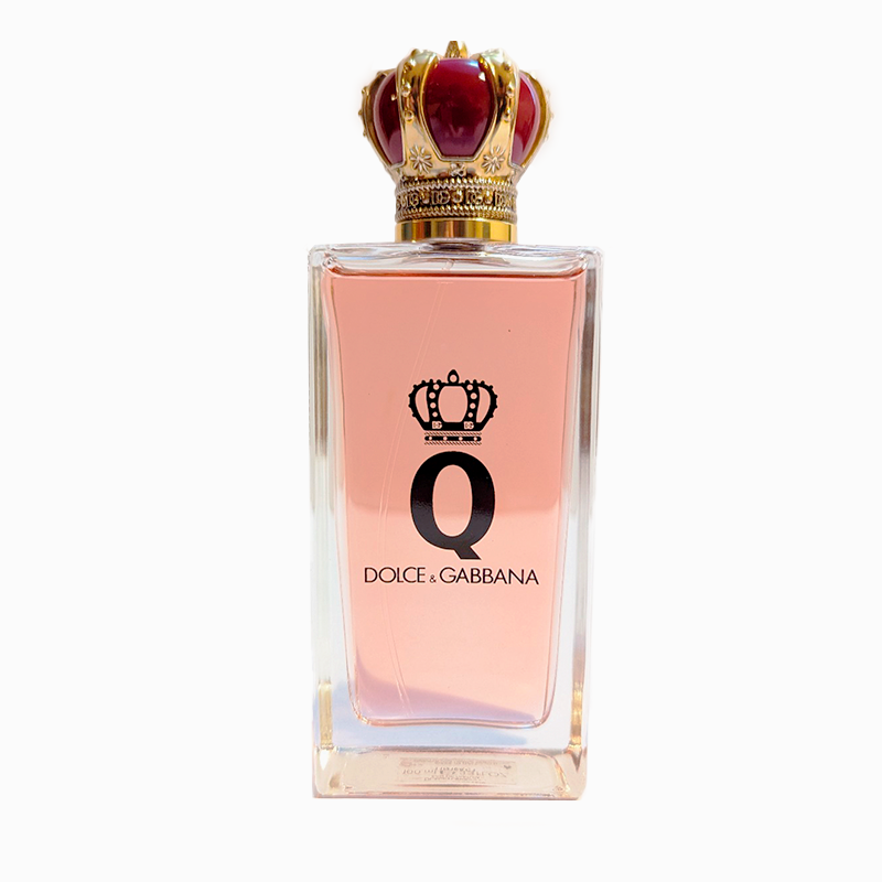 A clear glass bottle of Dolce & Gabbana perfume with a pink liquid inside, featuring a crown-shaped red and gold cap and the letter “Q” on the front.