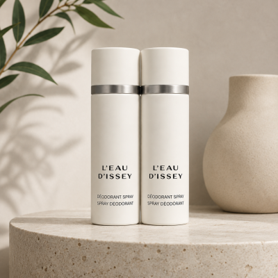 Two bottles of Issey Miyake L’eau D’Issey 100ml Deodorant Spray for Women stand side by side on a textured surface, with a beige vase and leafy branch in the background.