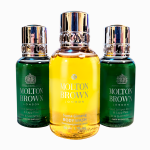 Three Molton Brown London bottles are displayed; two green bottles labeled "Bath & Shower" and a central yellow bottle labeled "Suma Ginseng Body Wash." All bottles have shiny metallic caps.