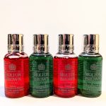 Four Molton Brown London bath and shower products are lined up, featuring two red and two green bottles with silver caps.