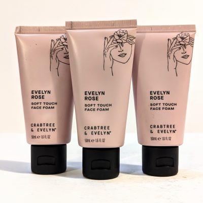 Three tubes of Crabtree & Evelyn Rose Soft Touch Face Foam with illustrations of a woman's face on a pink background.