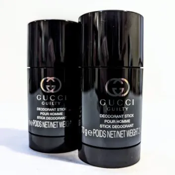 Two 75ml Gucci Guilty Deodorant Sticks for Men stand upright on a white surface, their shiny black packaging reflecting below.