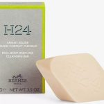 The Hermès H24 Face, Body, and Hair Cleansing Bar, 100g—a rectangular soap embossed with "H24"—is presented against its branded green and gray packaging.