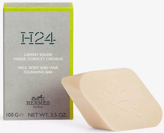 The Hermès H24 Face, Body, and Hair Cleansing Bar, 100g—a rectangular soap embossed with "H24"—is presented against its branded green and gray packaging.