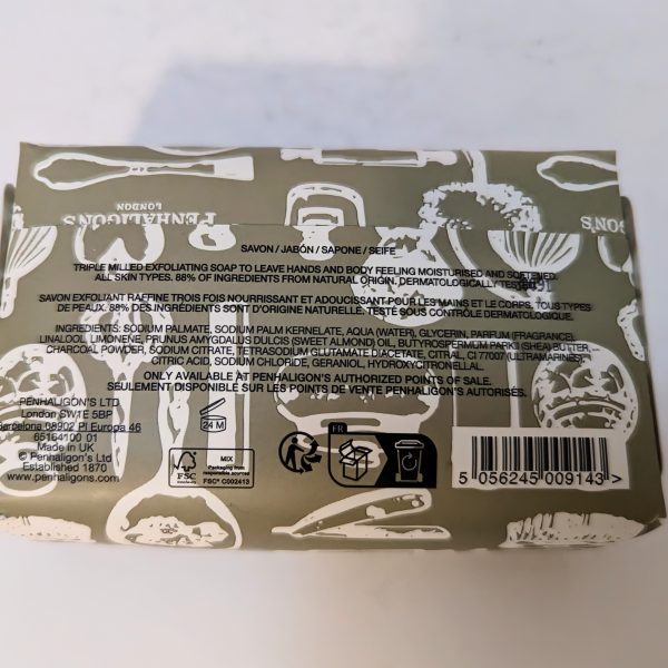 Back of a soap package with black text detailing product information, barcode, recycling symbols, and branding. The background is olive green with white illustrations of grooming tools.