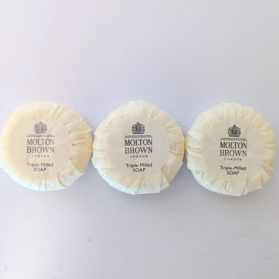 Three round, wrapped bars of Molton Brown London triple-milled soap are arranged side by side on a white surface.