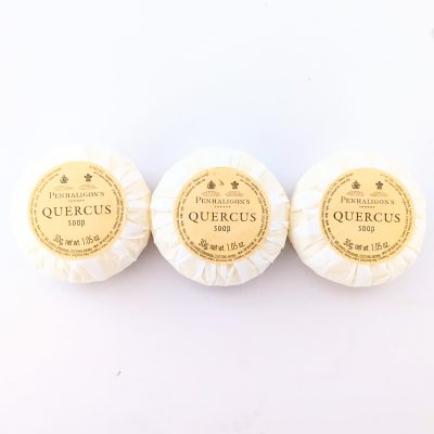 Three round, wrapped bars of Penhaligon’s Quercus soap, each with a yellow label, arranged in a horizontal row on a white background.