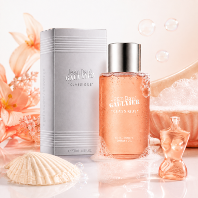 A bottle of Jean Paul Gaultier Classique Bath & Shower Gel, 200ml, is displayed alongside its box, surrounded by seashells, flowers, bubbles, and a small torso-shaped figurine on a white surface.