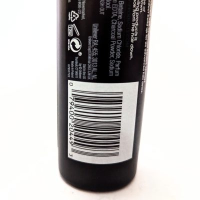 A close-up of a product label on a black bottle, showing a barcode, recycling symbols, ingredient list, and some text.
