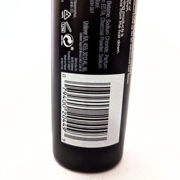 A close-up of a product label on a black bottle, showing a barcode, recycling symbols, ingredient list, and some text.