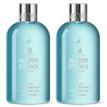 Two bottles of Molton Brown Coastal Cypress & Sea Fennel Bath and Shower Gel (300ml, unisex) with silver caps, clear blue liquid, and white labels stand side by side against a white background.