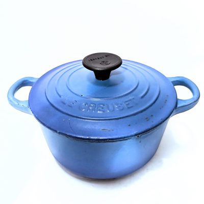 A blue Le Creuset cast iron Dutch oven with a black knob and two handles, shown on a white background.