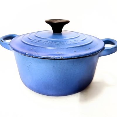 A blue Le Creuset cast iron Dutch oven with a lid and two handles, shown against a white background.