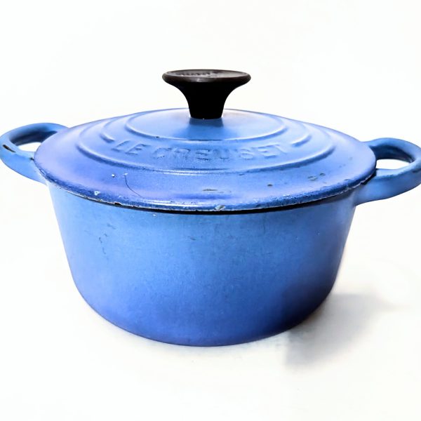 A blue cast-iron Le Creuset Dutch oven with a lid and black handle, shown against a plain white background.
