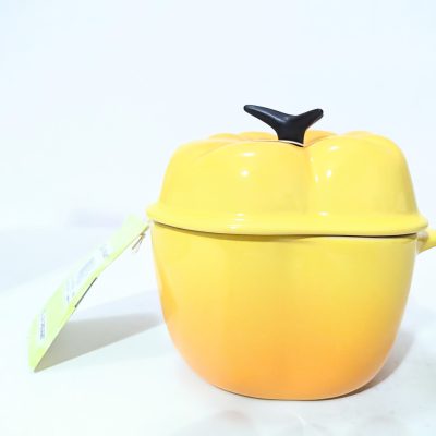 A yellow ceramic pot with a lid shaped like a pumpkin, featuring a stem-shaped handle and a tag attached to one side, placed against a plain background.