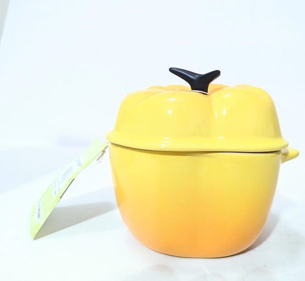 A yellow ceramic pot with a lid shaped like a pumpkin, featuring a stem-shaped handle and a tag attached to one side, placed against a plain background.