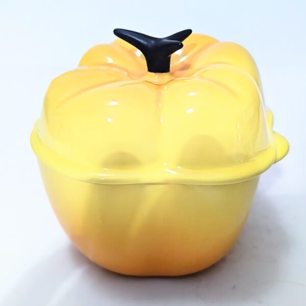 Yellow ceramic casserole dish shaped like a pumpkin with a black stem handle on the lid, shown on a plain white background.