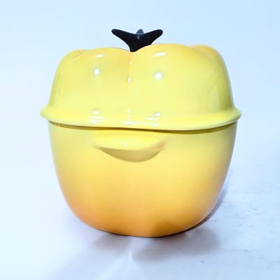 Yellow ceramic pot with a lid shaped like a bell pepper, featuring a small black handle on top, placed on a white surface.