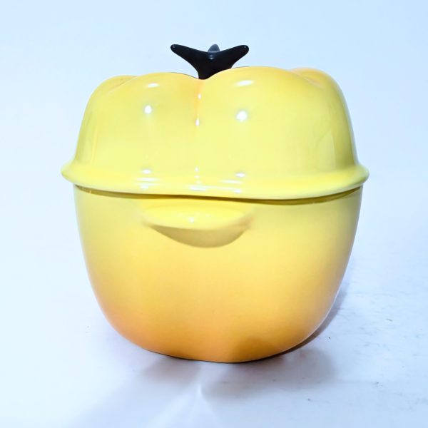 Yellow ceramic pot with a lid shaped like a bell pepper, featuring a small black handle on top, placed on a white surface.