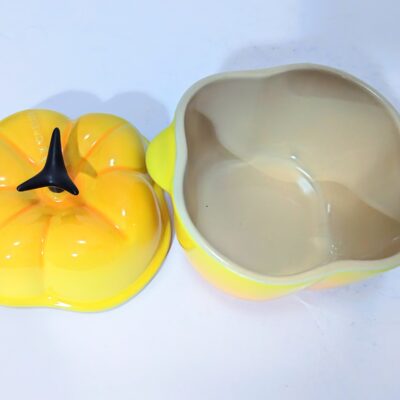A yellow, pumpkin-shaped ceramic dish with a matching lid placed beside it on a white surface.