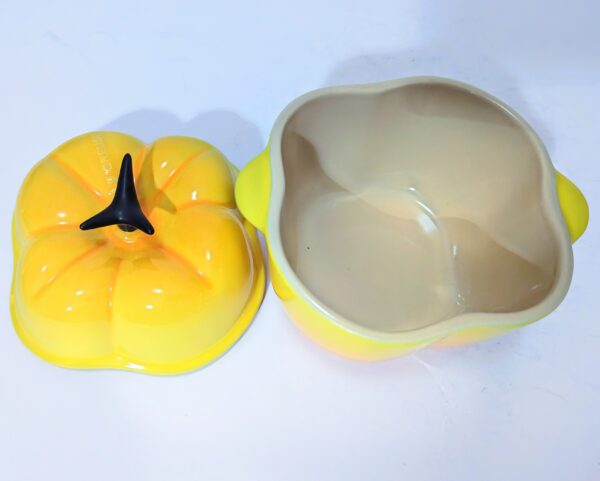 A yellow, pumpkin-shaped ceramic dish with a matching lid placed beside it on a white surface.