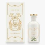The Gucci The Alchemist's Garden Love At Your Darkest EDP Spray (100ml Unisex) is displayed in a white bottle with gold accents beside its matching decorative box adorned with gold detailing and text.