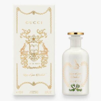The Gucci The Alchemist's Garden Love At Your Darkest EDP Spray (100ml Unisex) is displayed in a white bottle with gold accents beside its matching decorative box adorned with gold detailing and text.