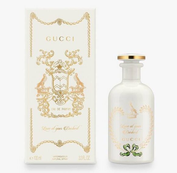 The Gucci The Alchemist's Garden Love At Your Darkest EDP Spray (100ml Unisex) is displayed in a white bottle with gold accents beside its matching decorative box adorned with gold detailing and text.