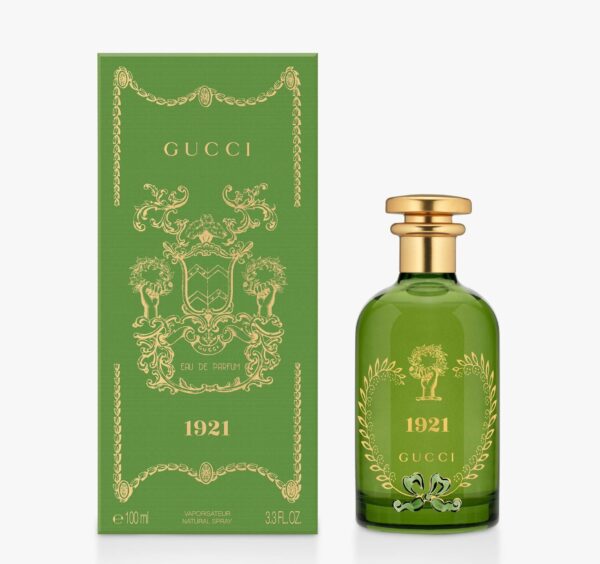 A green bottle of Gucci 1921 Eau de Parfum Spray, Unisex, 100ml is shown beside its decorative matching green and gold box. A green bottle of Gucci 1921 Eau de Parfum Spray, Unisex, 100ml is shown beside its decorative matching green and gold box.