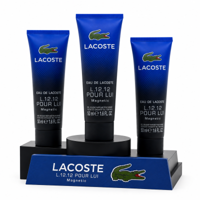 Three blue Lacoste Eau de Lacoste L.12.12 Pour Lui Magnetic 50ml shower gels displayed on a branded stand with white text and a green crocodile logo.