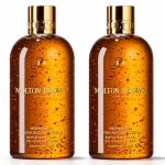 Two bottles of Molton Brown Mesmerising Oudh Accord & Gold Bath & Shower Gel, 300ml each, are shown side by side against a white background. Each features a gold cap and contains suspended gold flakes.