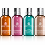 The Molton Brown Woody & Floral Body Care Shower Gel Collection (4x 100ml) features four bottles in a row, each with a unique color and label: black pepper, pink pepper, cypress & sea fennel, and rhubarb & rose.