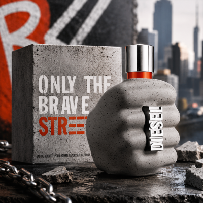 A concrete-textured perfume bottle shaped like a fist is displayed in front of a matching box labeled "Diesel Only The Brave Street EDT Spray for Men, 50ml," with a city skyline visible in the blurred background.