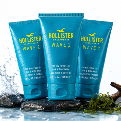 Two blue tubes of 2x Hollister Wave 2 Shower Gel Body Wash for Men, 100ml, stand upright on wet stones with water splashing and seaweed nearby.