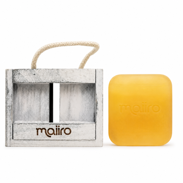 A yellow rectangular soap bar with “maiiro” embossed, next to a white wooden holder with a rope handle and the same brand name.