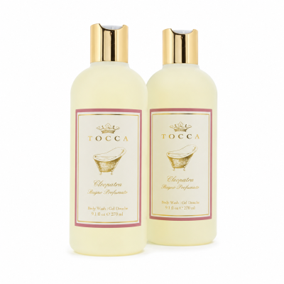 Two bottles of Tocca Cleopatra body wash with gold caps, white labels, and a gold bathtub illustration are displayed side by side on a white background.
