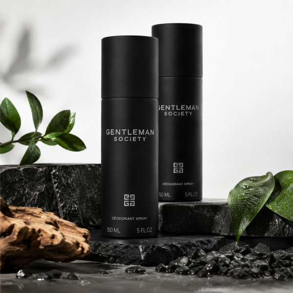 Two bottles of Givenchy Gentleman Society Deodorant Spray for men (150ml each) are displayed on a slate surface, accompanied by green leaves and a piece of wood.