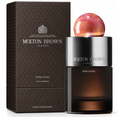 A bottle of Molton Brown Rose Dunes EDP 100ml, Unisex stands beside its textured brown box. The bottle features a round, pink marbled cap and metallic accents.