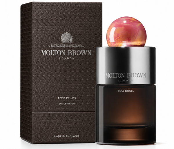A bottle of Molton Brown Rose Dunes EDP 100ml, Unisex stands beside its textured brown box. The bottle features a round, pink marbled cap and metallic accents.