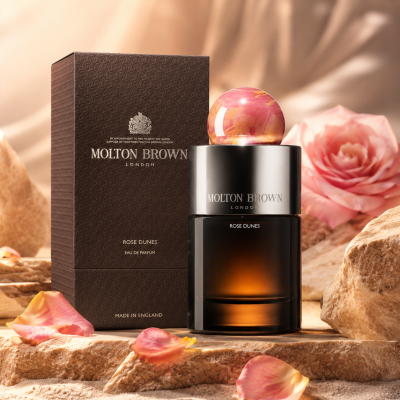 Molton Brown Rose Dunes EDP 100ml (Unisex) bottle and box displayed among pink rose petals and sandy rocks.