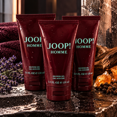 Three tubes of JOOP! HOMME shower gel stand on a wet stone surface, surrounded by lavender, amber stones, and dark towels in the background.