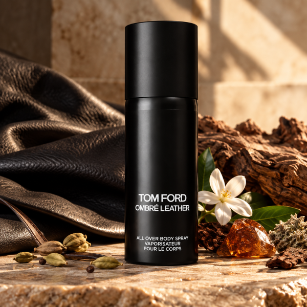 Two black canisters of 2x Tom Ford Ombré Leather Body Spray, Unisex, 150ml stand on stone with spices, amber, a white flower, and leather fabric in the background.