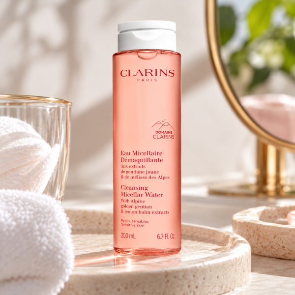 A bottle of 3x Clarins Cleansing Micellar Water 200ml with pink liquid, standing on a stone vanity tray next to a folded white cloth.