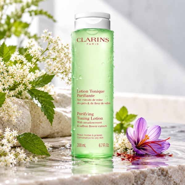 3x Clarins Purifying Toning Face Lotion 200ml in a green bottle for combination to oily skin, sitting on a wet surface with a saffron flower and white blossoms.